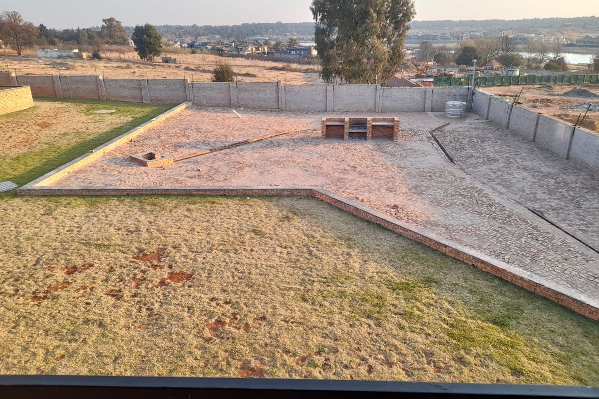 Spacious rear yard featuring a paved area, built-in brick braai, and perimeter walling, offering potential for landscaping and outdoor entertainment development.