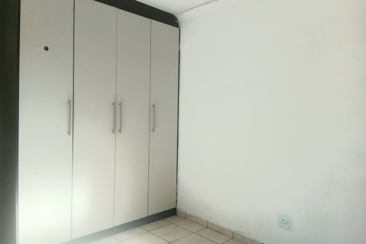 A vacant bedroom featuring built-in cupboards and tiled flooring, showing signs of minor wear on the walls and ceiling.