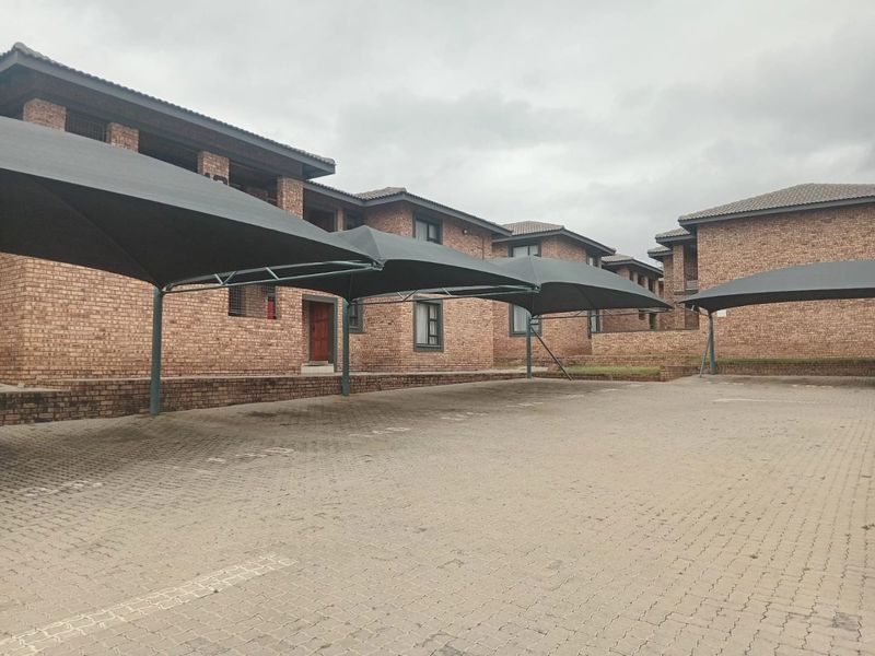 Exterior view of an apartment complex featuring face-brick architecture, paved parking area, and installed shade cloth carports.
