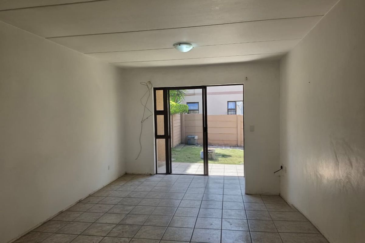 An empty, tiled living room featuring a sliding glass door that opens to a small rear garden area.