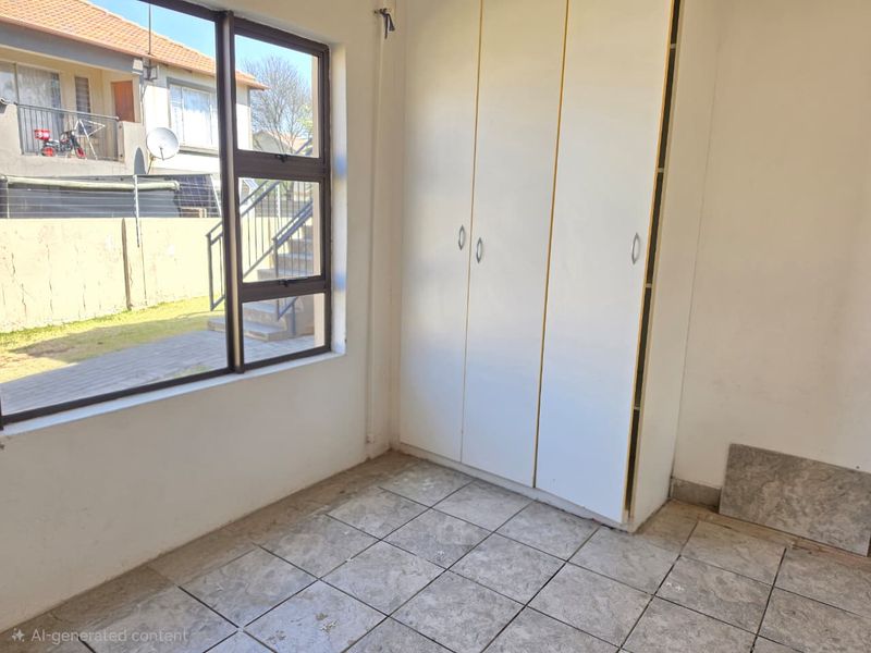 An empty bedroom featuring tiled flooring, built-in cupboards, and a large window overlooking the exterior area.