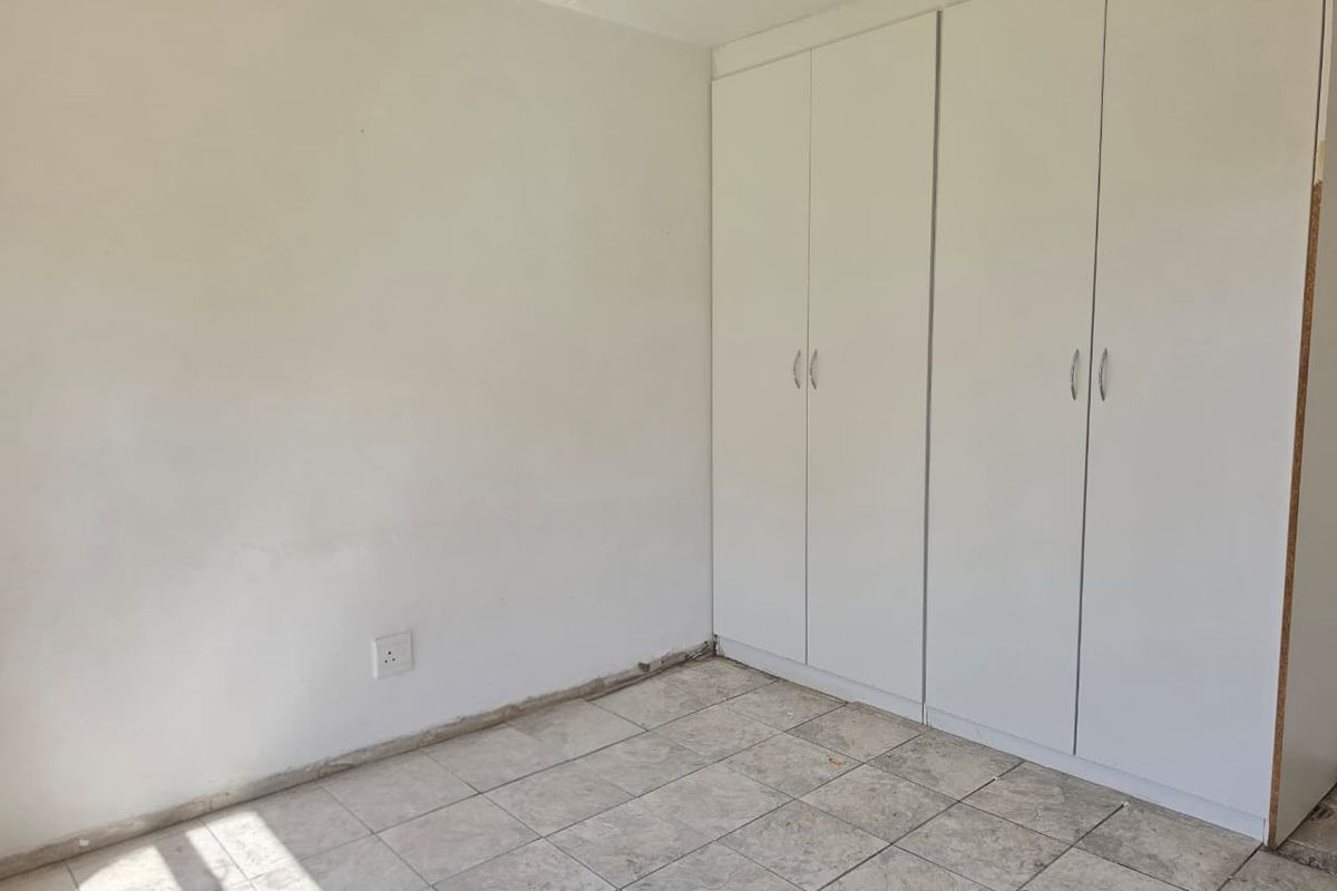 An empty bedroom featuring white built-in cupboards and tiled flooring, requiring minor finishing touches like skirting boards to complete the space.