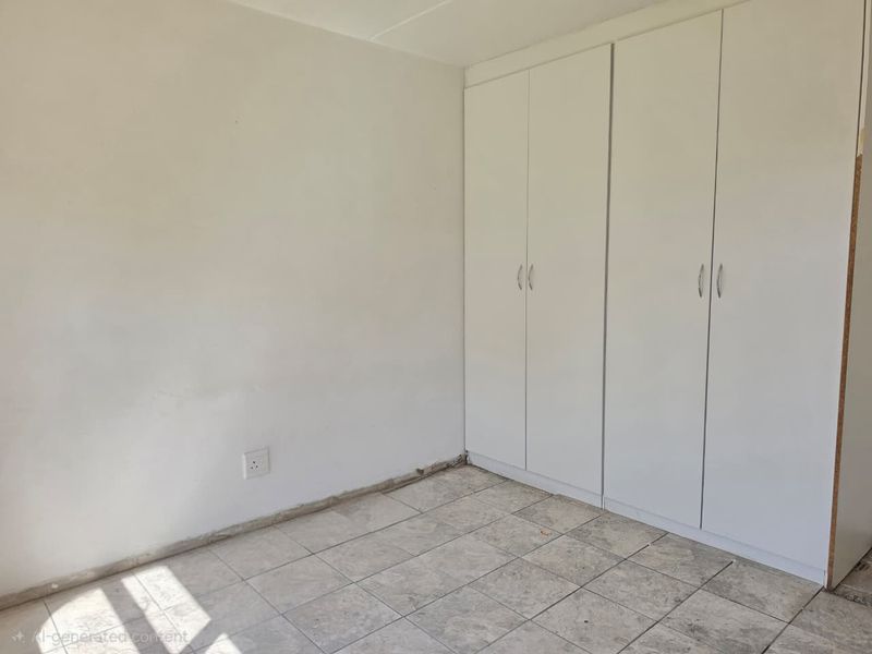 An empty bedroom featuring white built-in cupboards and tiled flooring, requiring minor finishing touches like skirting boards to complete the space.