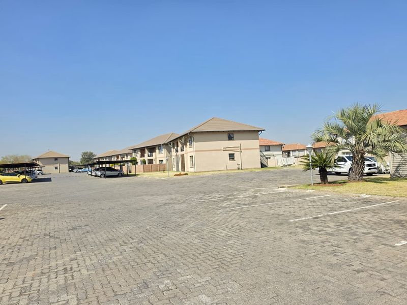 Exterior view of an apartment complex featuring a large paved parking area with covered parking bays and multi-story residential units.