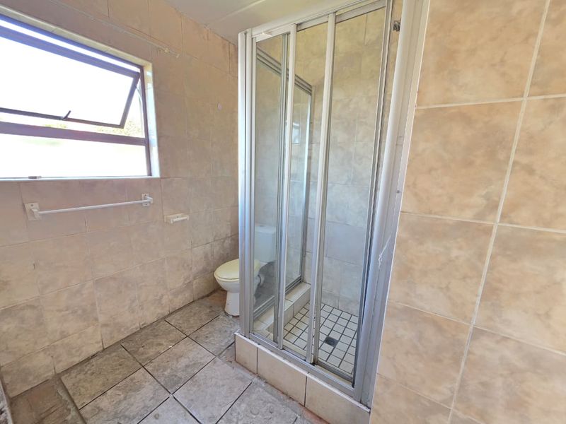 A dated bathroom featuring a shower enclosure, toilet, and tiled finishes throughout, requiring cosmetic updates to improve its overall condition and appeal.