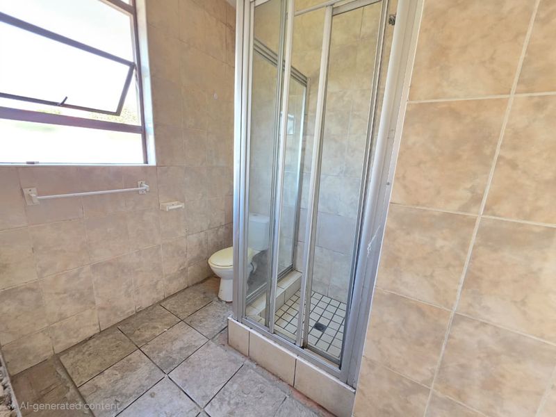 A functional bathroom featuring a shower enclosure, toilet, and tiled finishes throughout, offering a blank canvas for potential renovation and modernization.