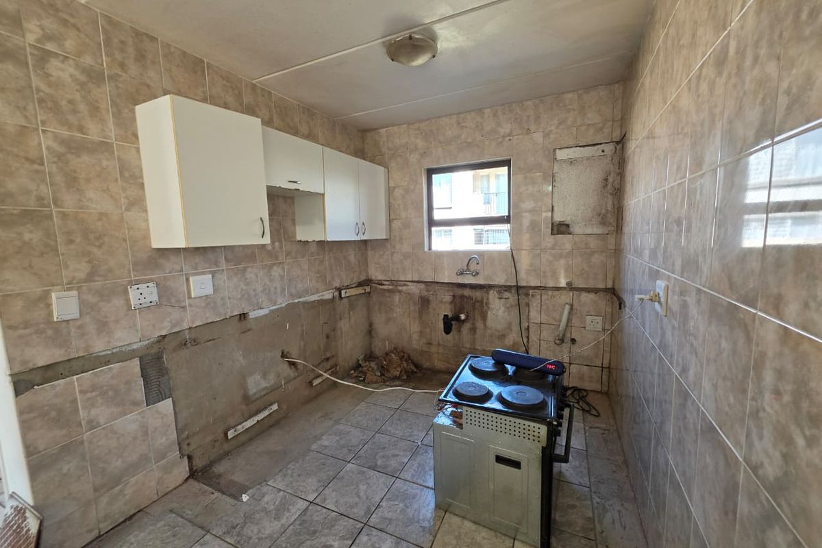 A partially renovated kitchen featuring tiled surfaces and wall-mounted cabinetry, currently requiring completion of cabinetry and wall finishes.