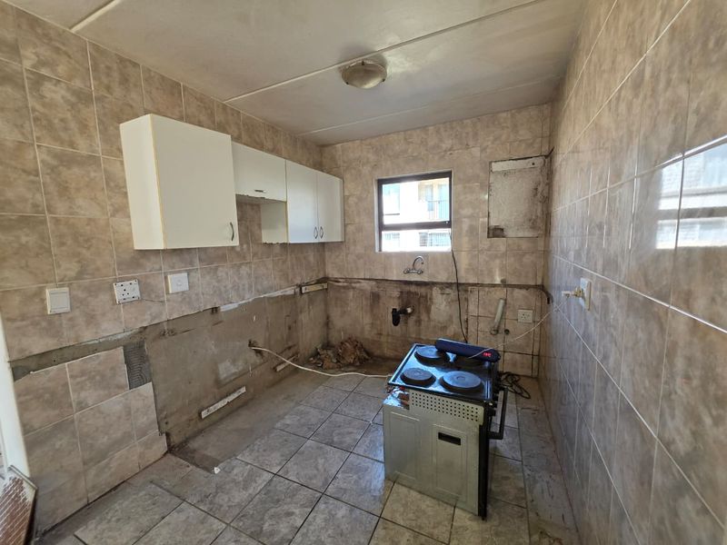 A partially renovated kitchen featuring tiled surfaces and wall-mounted cabinetry, currently requiring completion of cabinetry and wall finishes.