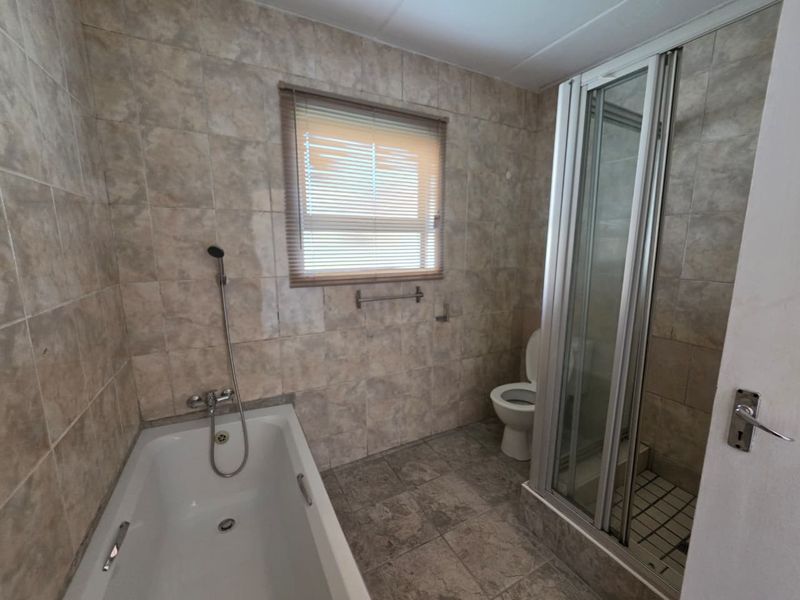 A functional bathroom featuring a bathtub, separate shower enclosure, and toilet, finished with neutral wall and floor tiling.
