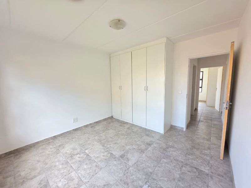 A bright, empty bedroom featuring neutral tiled flooring and white built-in cupboards, offering a clean and versatile space.