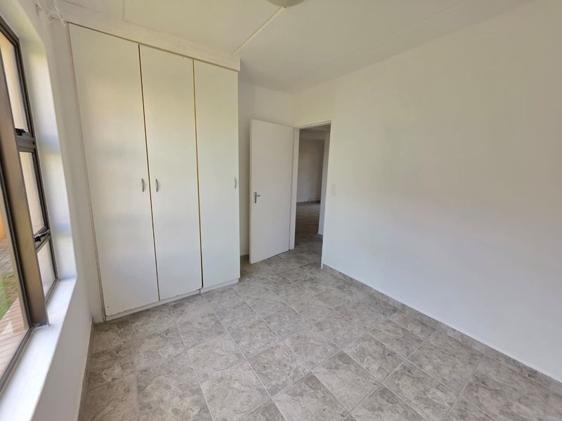 A bright, empty bedroom featuring neutral tiled flooring and built-in cupboards, offering a clean canvas for personalization.