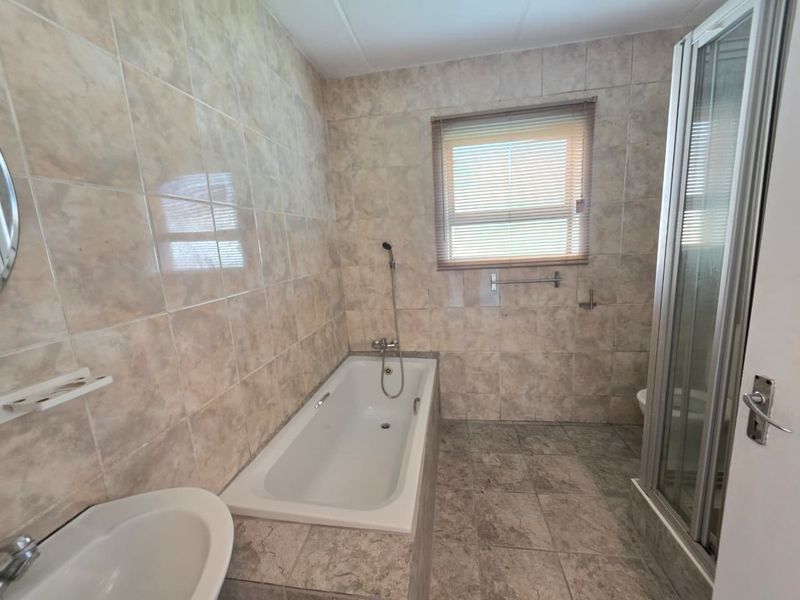 A functional bathroom featuring a built-in bathtub, separate shower enclosure, and pedestal washbasin with neutral ceramic wall and floor tiling.