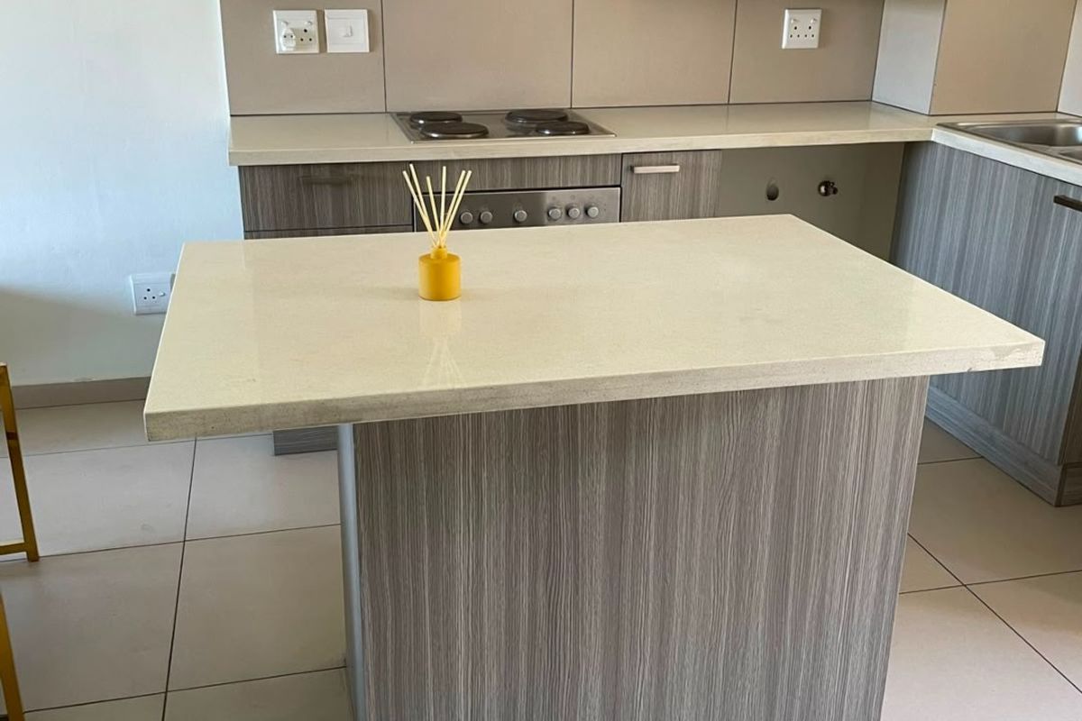 Modern kitchen featuring wood-grain cabinetry, stone countertops, a central island, and integrated appliances including an electric hob and extractor fan.