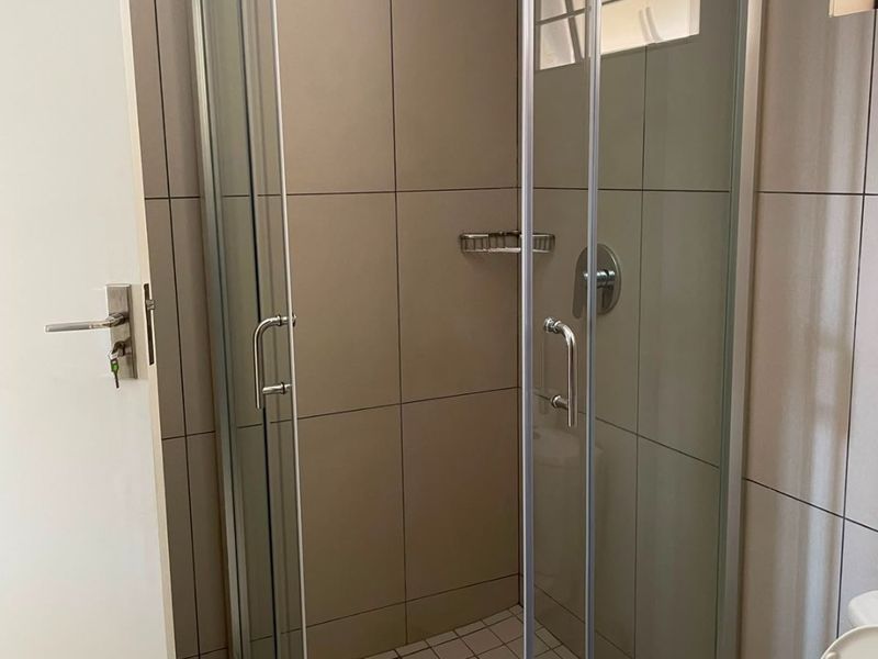 A clean bathroom featuring a glass-enclosed shower with neutral wall tiling and a standard toilet.