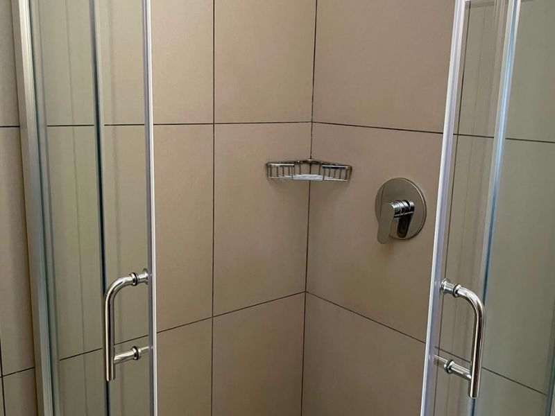 A clean, modern shower stall featuring neutral wall tiles, a glass enclosure, and a built-in corner caddy.