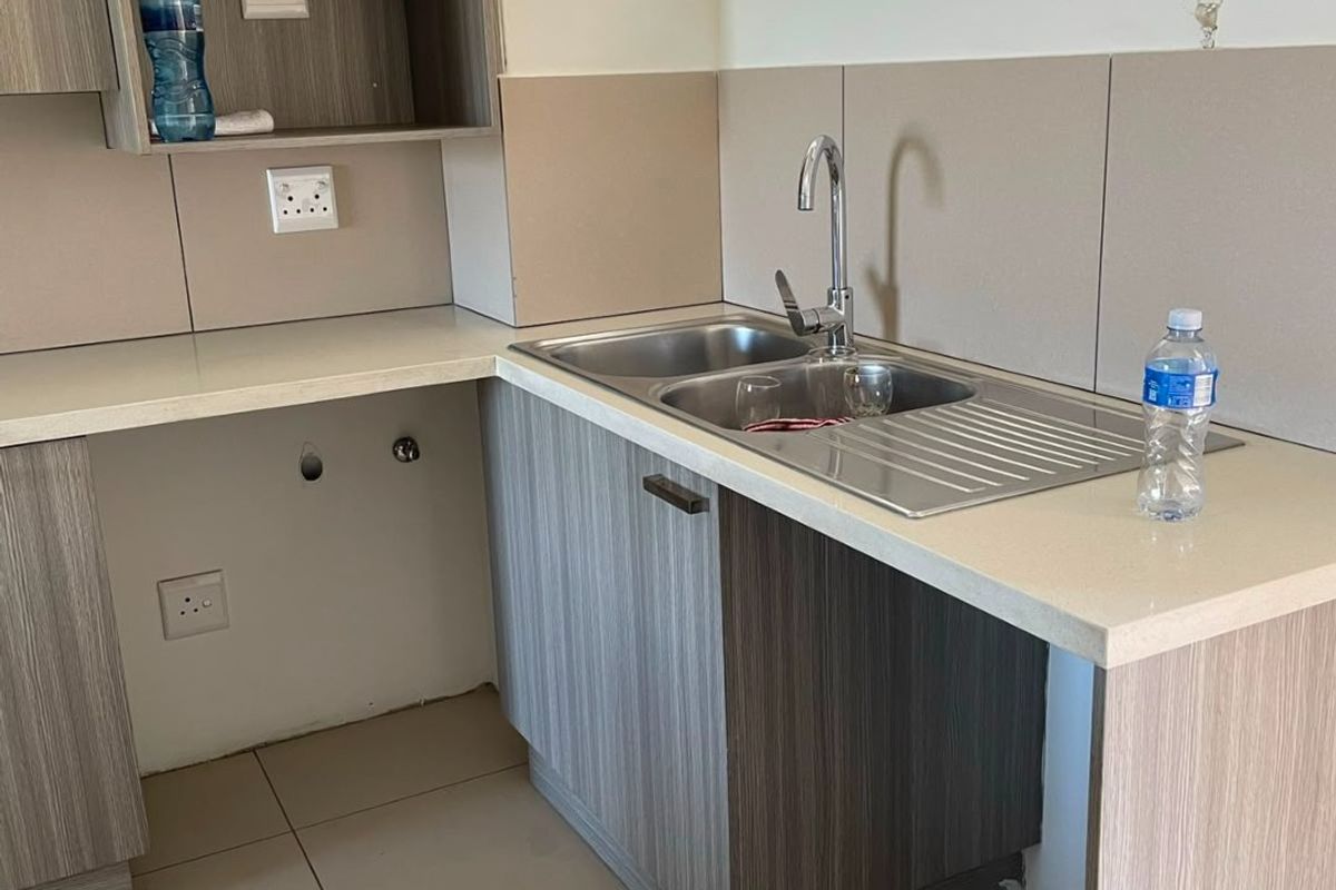A compact kitchen area featuring modern laminate cabinetry, stone countertops, a stainless steel sink, and tiled splashbacks, ready for appliance installation.