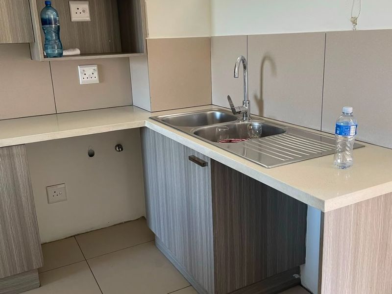A compact kitchen area featuring modern laminate cabinetry, stone countertops, a stainless steel sink, and tiled splashbacks, ready for appliance installation.