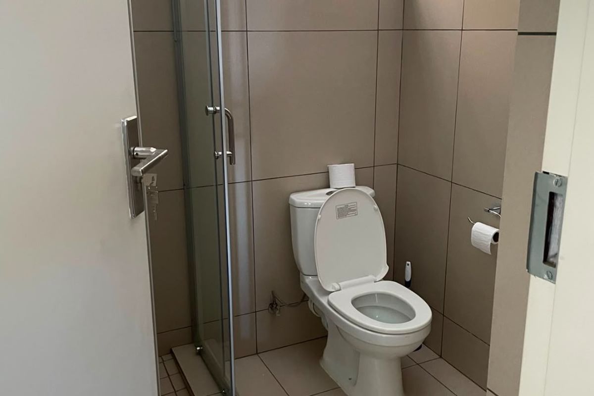 A compact, modern bathroom featuring neutral floor-to-ceiling tiling, a glass shower enclosure, and a standard toilet.