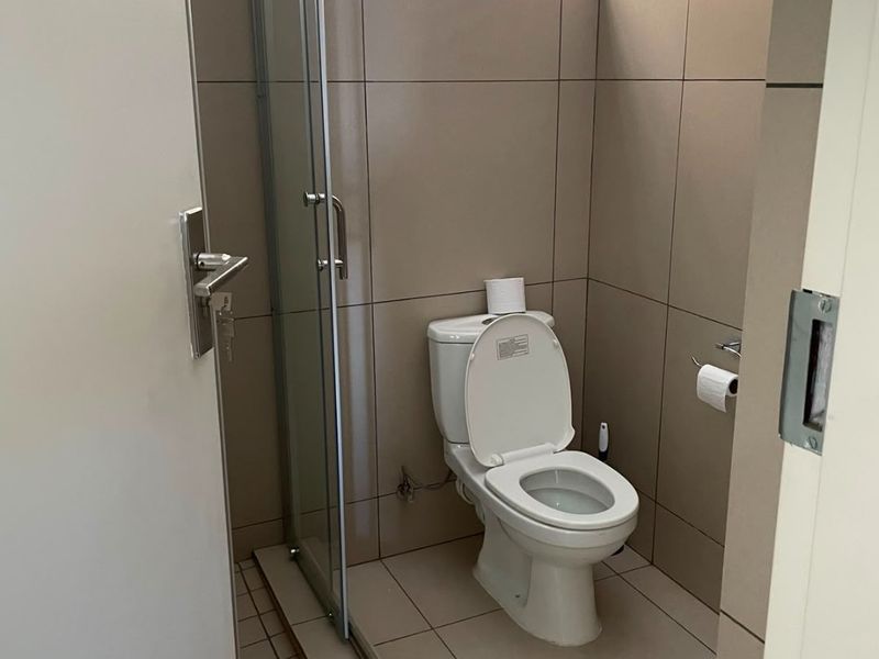 A compact, modern bathroom featuring neutral floor-to-ceiling tiling, a glass shower enclosure, and a standard toilet.