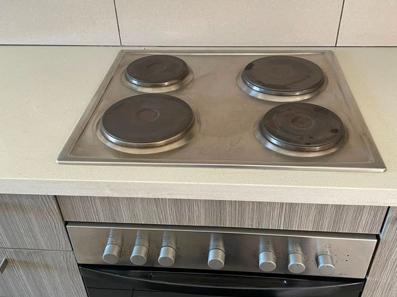 A close-up view of a kitchen featuring a built-in oven, electric hob, stone countertop, and modern laminate cabinetry with a tiled backsplash.