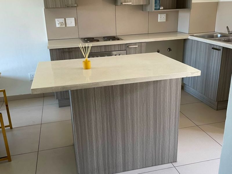 Modern kitchen featuring wood-grain cabinetry, stone countertops, a central island, and integrated hob with extractor fan, set against neutral tiled flooring.