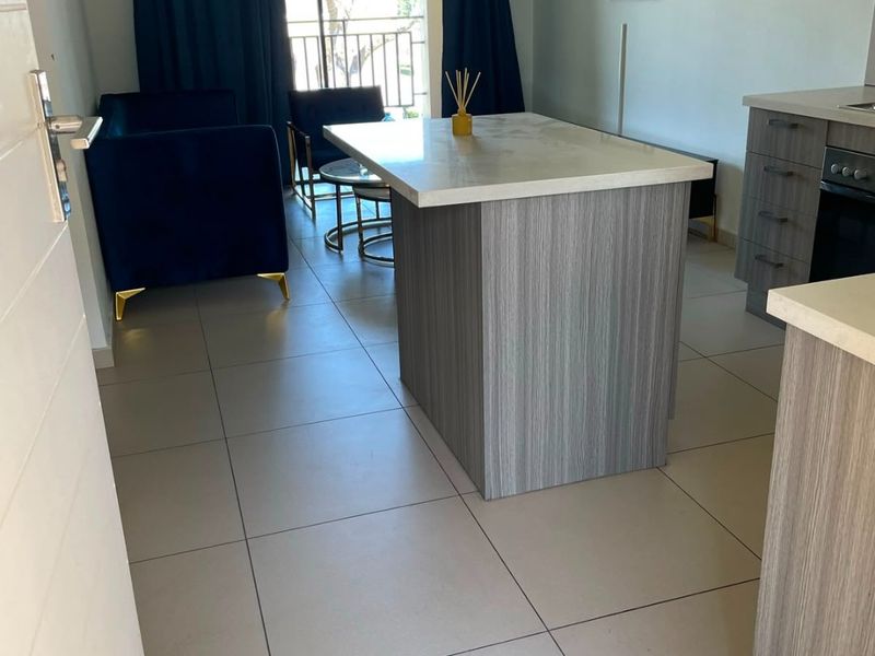 Open-plan living area featuring a modern kitchen island, tiled flooring, and direct access to a private balcony through sliding glass doors.