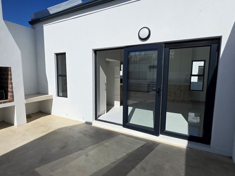 A clean outdoor patio area featuring a built-in brick braai, concrete flooring, and modern sliding glass doors leading into the home.