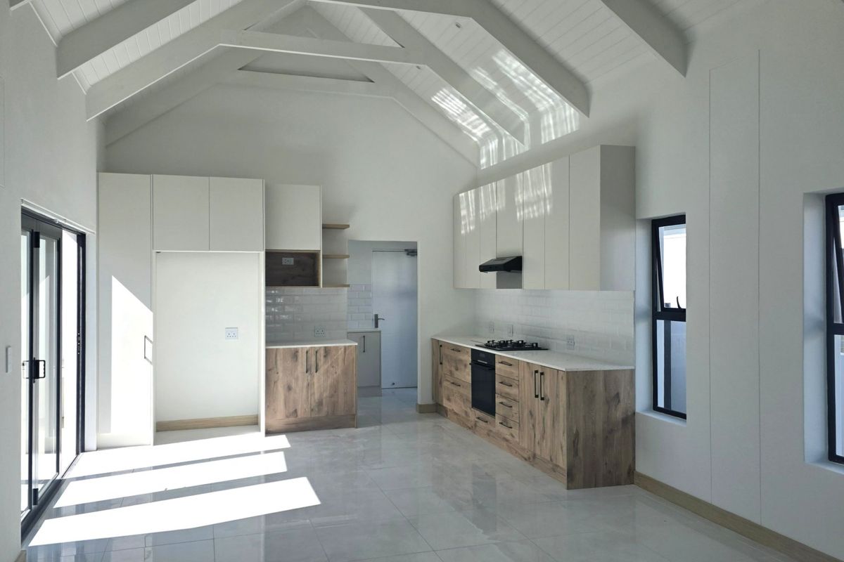 Modern kitchen featuring vaulted ceilings with exposed rafters, sleek two-tone cabinetry, stone countertops, integrated appliances, and large sliding doors leading to the exterior.