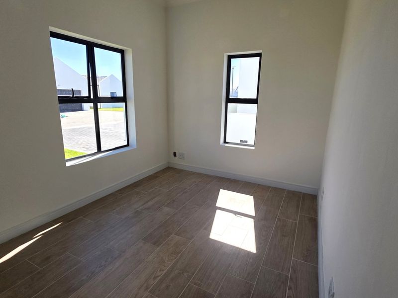 A bright, empty bedroom featuring modern wood-look tiled flooring and large aluminium-framed windows, offering a clean and neutral canvas.
