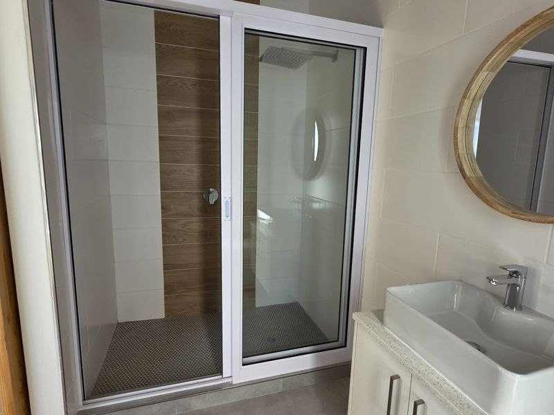 Modern bathroom featuring a walk-in shower with sliding glass doors, wood-look accent tiling, and a contemporary vanity with a countertop basin.
