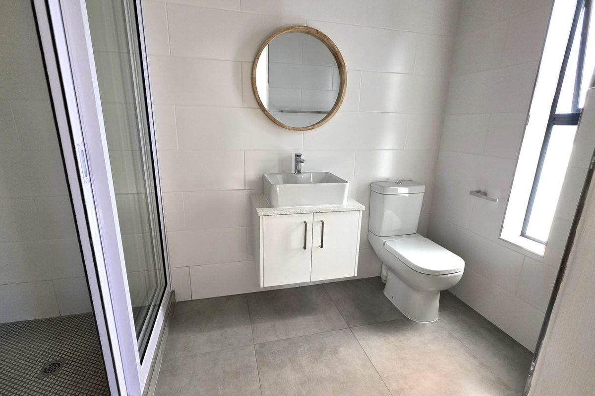 A modern, clean bathroom featuring a wall-mounted vanity with a vessel sink, a toilet, and a glass-enclosed shower with neutral tiled finishes.