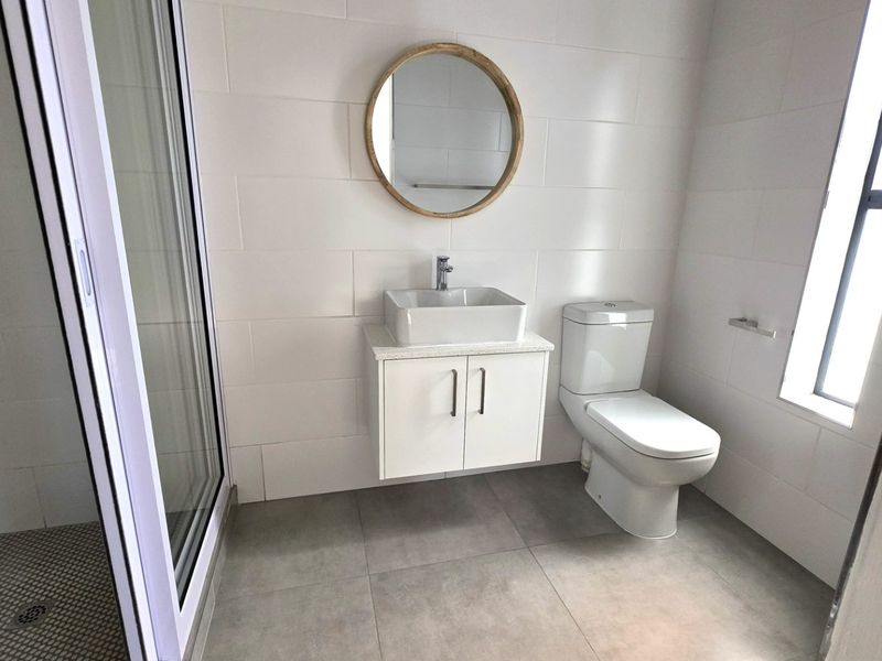 A modern, clean bathroom featuring a wall-mounted vanity with a vessel sink, a toilet, and a glass-enclosed shower with neutral tiled finishes.