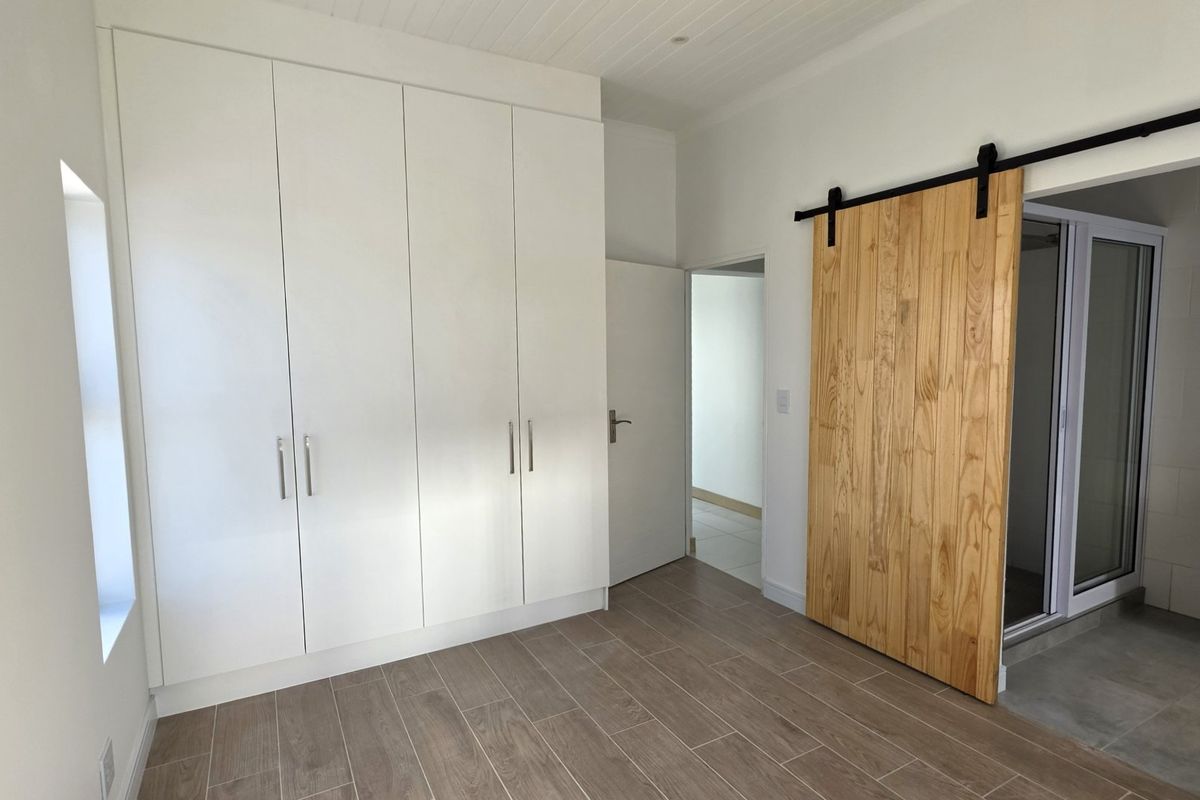 A bright, empty bedroom featuring modern built-in cupboards, wood-look tiled flooring, and a rustic sliding barn door leading to an adjoining space.