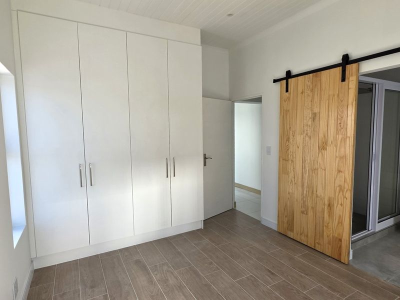 A bright, empty bedroom featuring modern built-in cupboards, wood-look tiled flooring, and a rustic sliding barn door leading to an adjoining space.