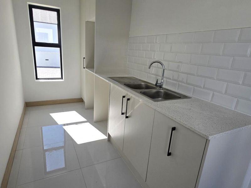 A clean, modern scullery featuring stone countertops, a double basin sink, subway tile backsplash, and ample built-in cabinetry.