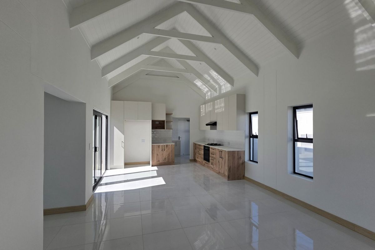 Spacious open-plan living and kitchen area featuring a high vaulted ceiling with exposed rafters, modern cabinetry, and sleek tiled flooring.