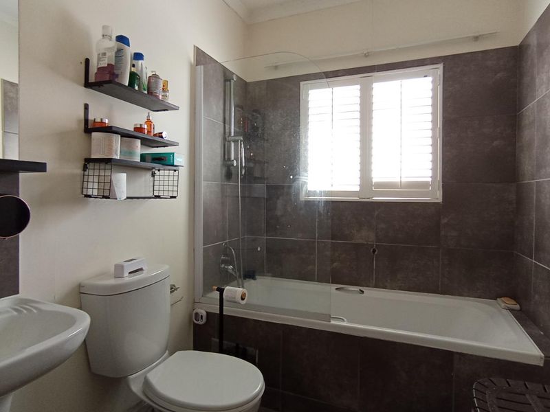 A functional bathroom featuring a pedestal basin, toilet, and a bathtub with a glass shower screen and tiled wall finishes.