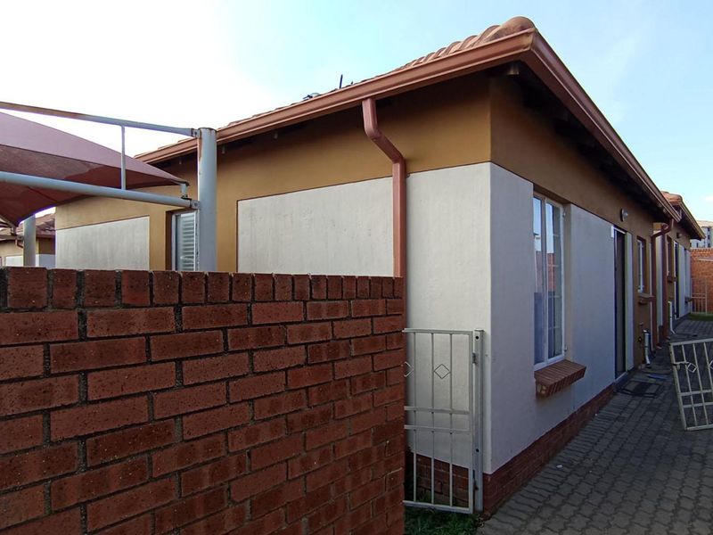Rear exterior view of the property featuring a paved walkway, brick boundary wall, and a shade sail structure over the side area.
