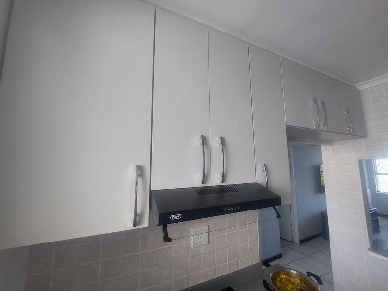 A functional kitchen area featuring white built-in cabinetry, a black extractor fan, and neutral tiled backsplash.