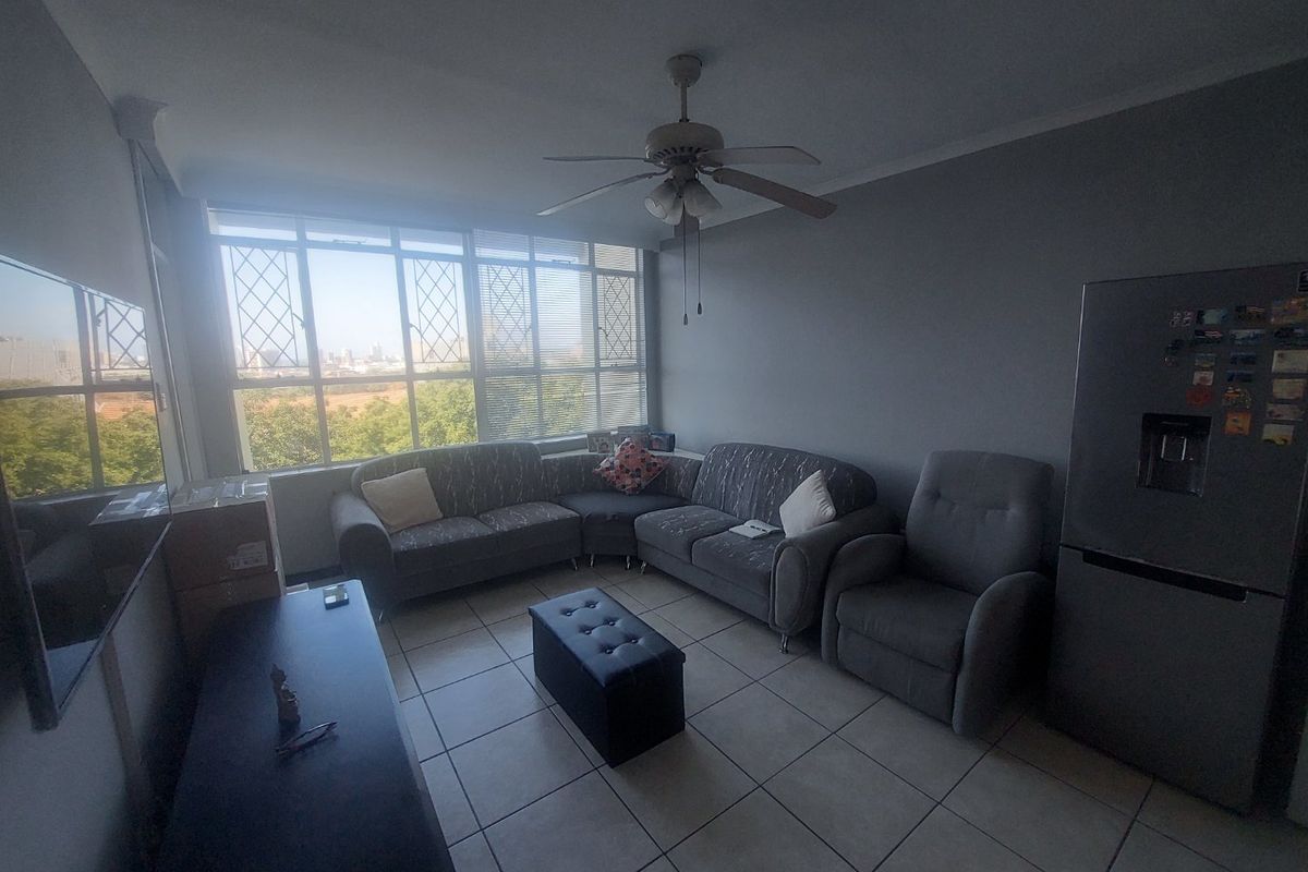 A living room featuring tiled flooring, a ceiling fan, and large windows providing natural light and an exterior view.
