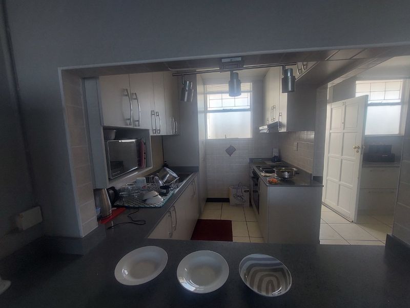 A functional kitchen featuring built-in cabinetry, tiled backsplash, and integrated appliances, viewed from an adjacent breakfast bar area.