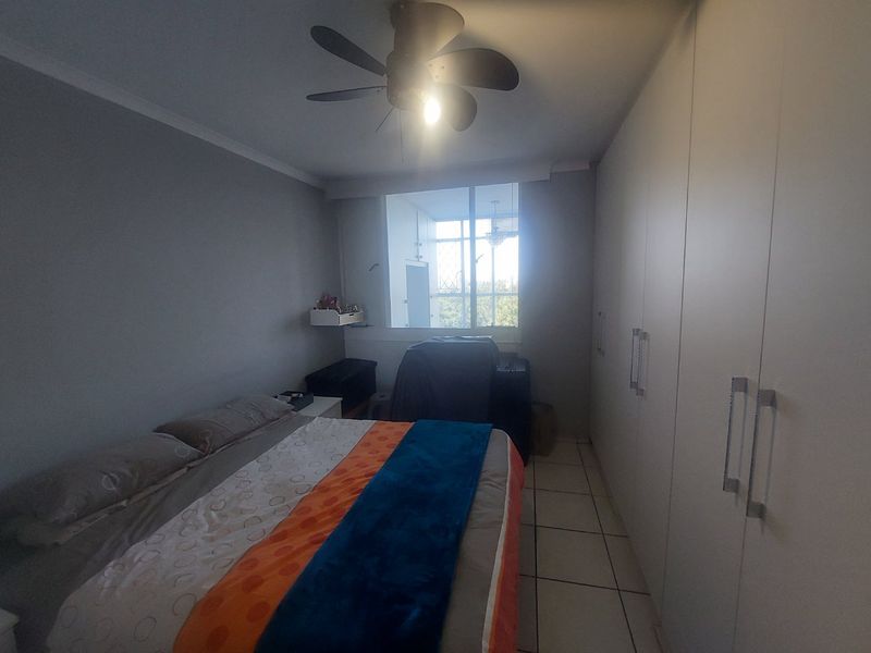 A bedroom featuring built-in cupboards, tiled flooring, and a ceiling fan, providing functional storage and basic amenities.