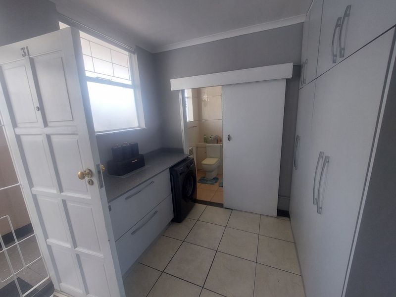 A functional laundry area featuring built-in cabinetry, tiled flooring, and direct access to an adjoining bathroom.