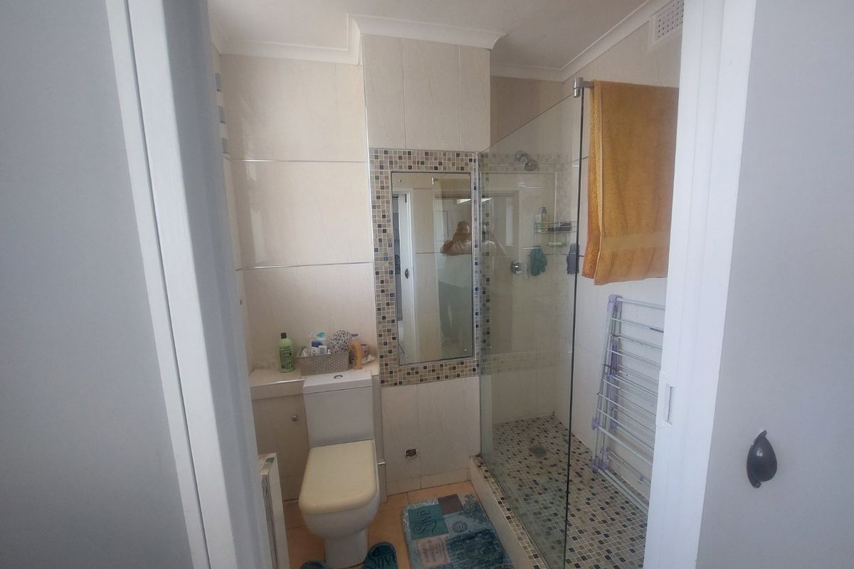 A functional bathroom featuring a glass-enclosed shower, tiled walls and flooring, and a built-in mirror.