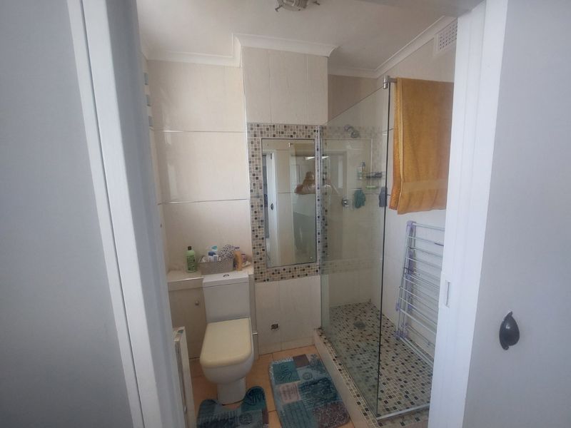 A functional bathroom featuring a glass-enclosed shower, tiled walls and flooring, and a built-in mirror.