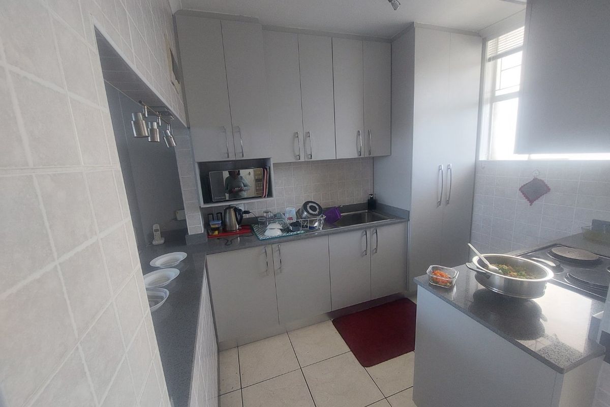 A functional kitchen featuring grey built-in cabinetry, stone countertops, tiled backsplash, and tiled flooring with a dedicated hob and microwave nook.