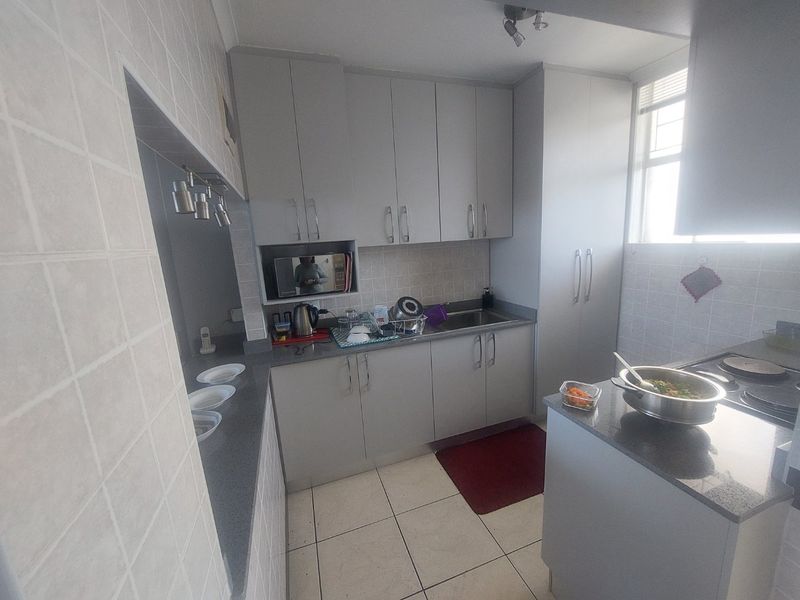 A functional kitchen featuring grey built-in cabinetry, stone countertops, tiled backsplash, and tiled flooring with a dedicated hob and microwave nook.