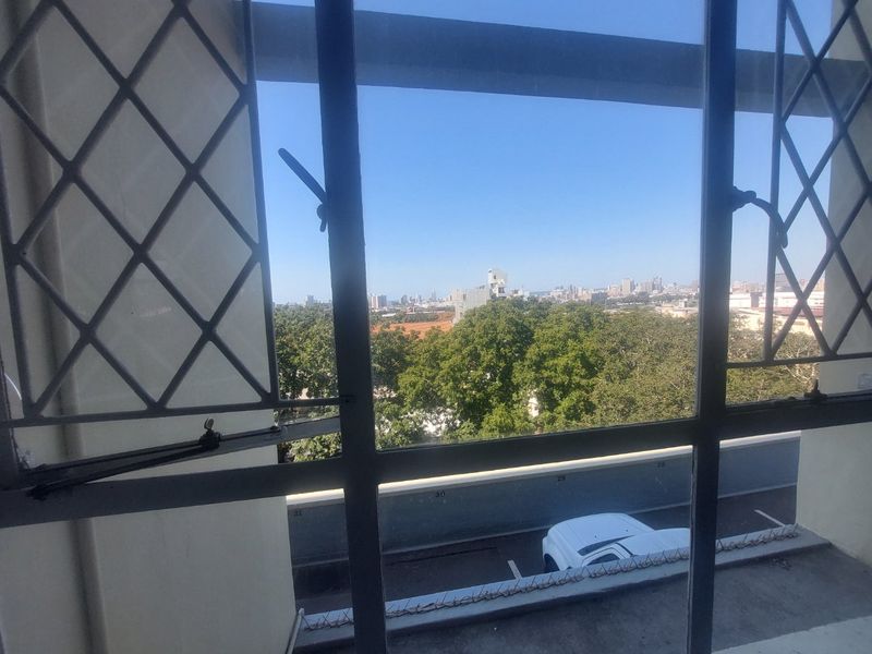 A view from an apartment window overlooking trees, a parking area, and the distant city skyline.