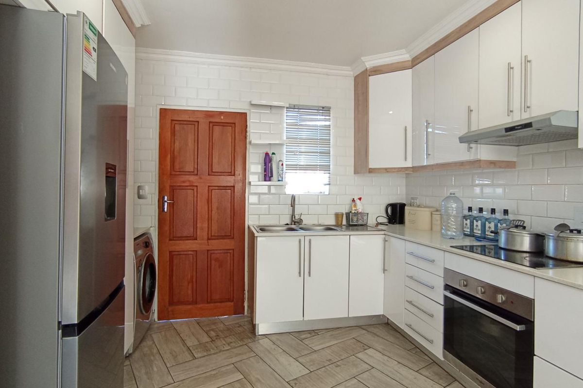 Modern kitchen featuring white cabinetry, subway tile backsplash, built-in oven with hob, and durable wood-look floor tiles.