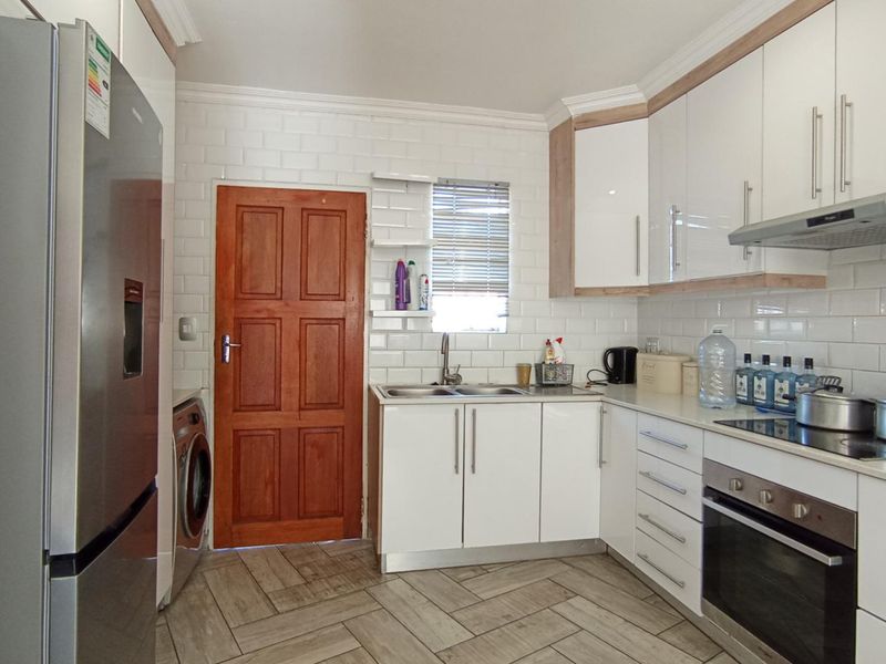 Modern kitchen featuring white cabinetry, subway tile backsplash, built-in oven with hob, and durable wood-look floor tiles.